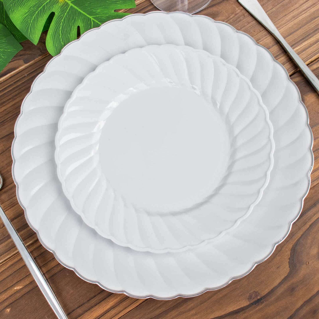 White scalloped dinner plates stacked on a wooden table.