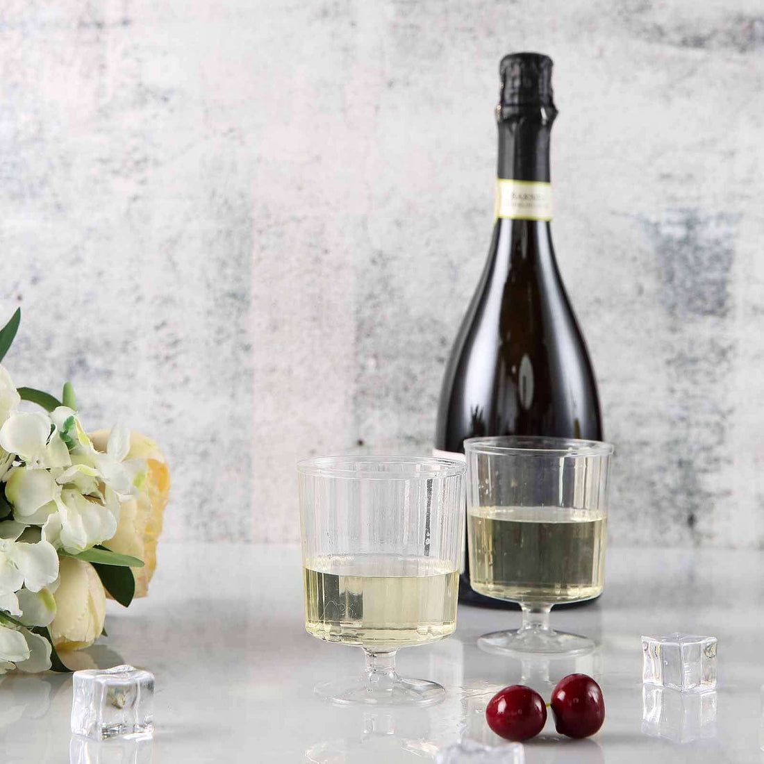 Chilled champagne bottle with glasses, ice cubes, and cherries on a textured background.
