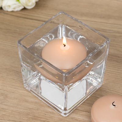 Square glass candle holder with a lit peach-colored candle inside.