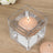 Square glass candle holder with a lit peach-colored candle inside.