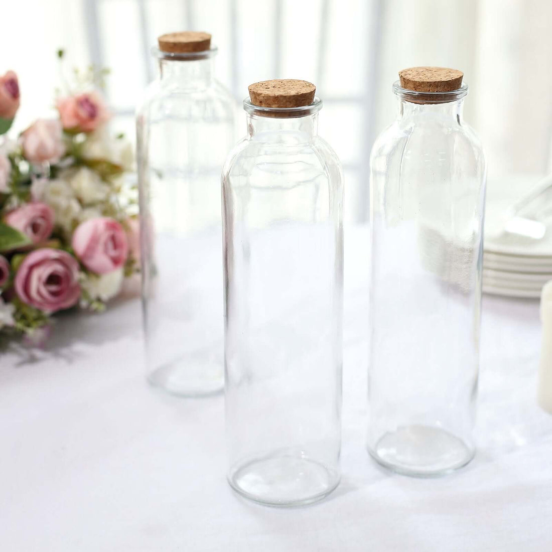 Clear glass bottles with cork lids on a table setting.