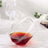 Geometric glass tumbler with red liquid, elegantly tilted on a soft surface.