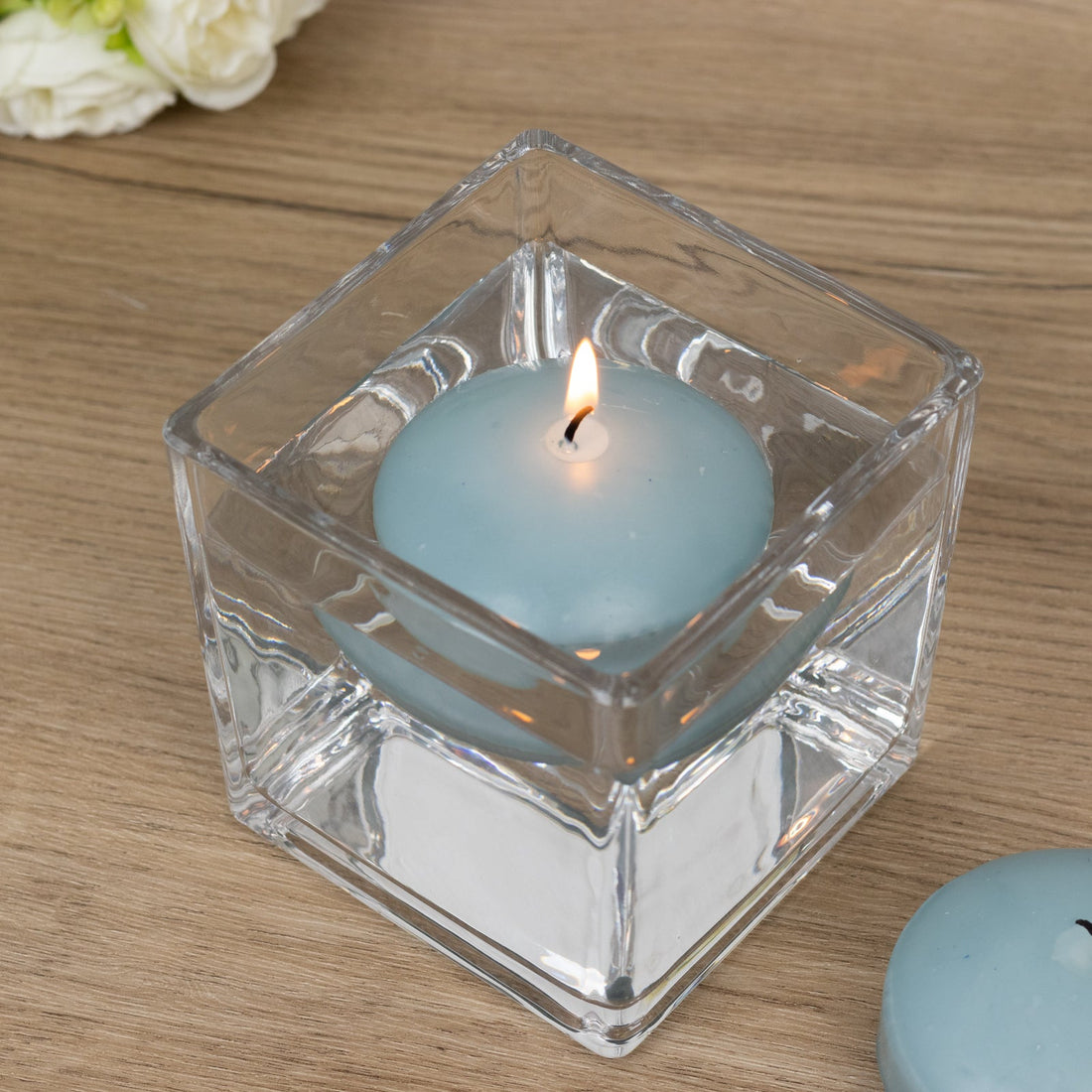 Blue candle in a clear glass holder with a lit wick.