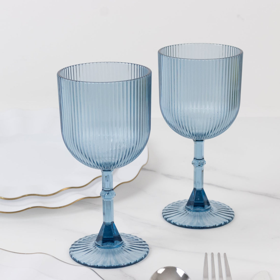 Two blue ribbed glass goblets on a marble table.