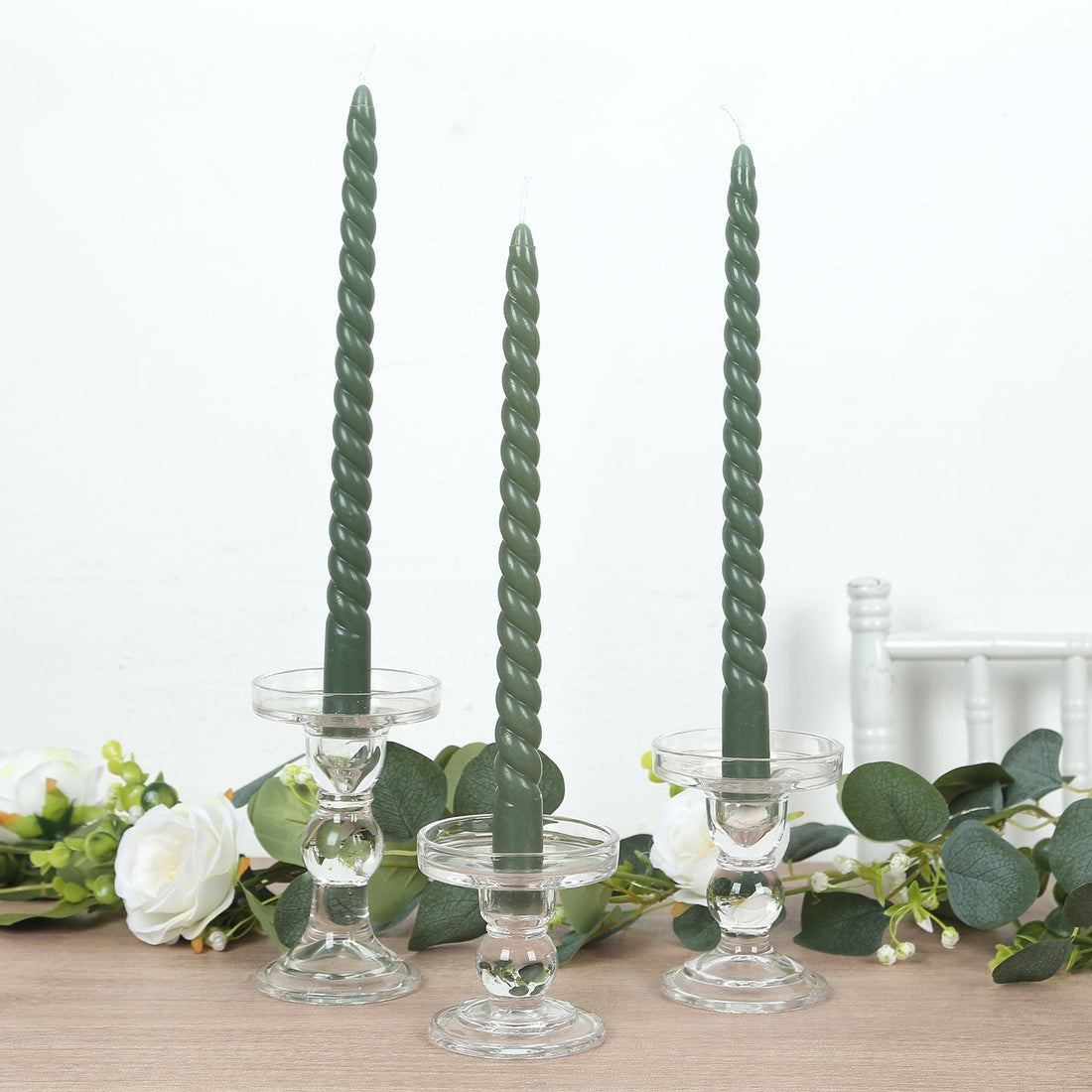 Twisted green candles in clear glass holders on a wooden table.