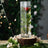 Clear glass vase filled with greenery and flowers on a wooden base.