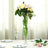 Tall floral arrangement in a clear vase on a dining table.