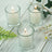 Set of three glass candles with lit wicks on a rustic wooden surface.