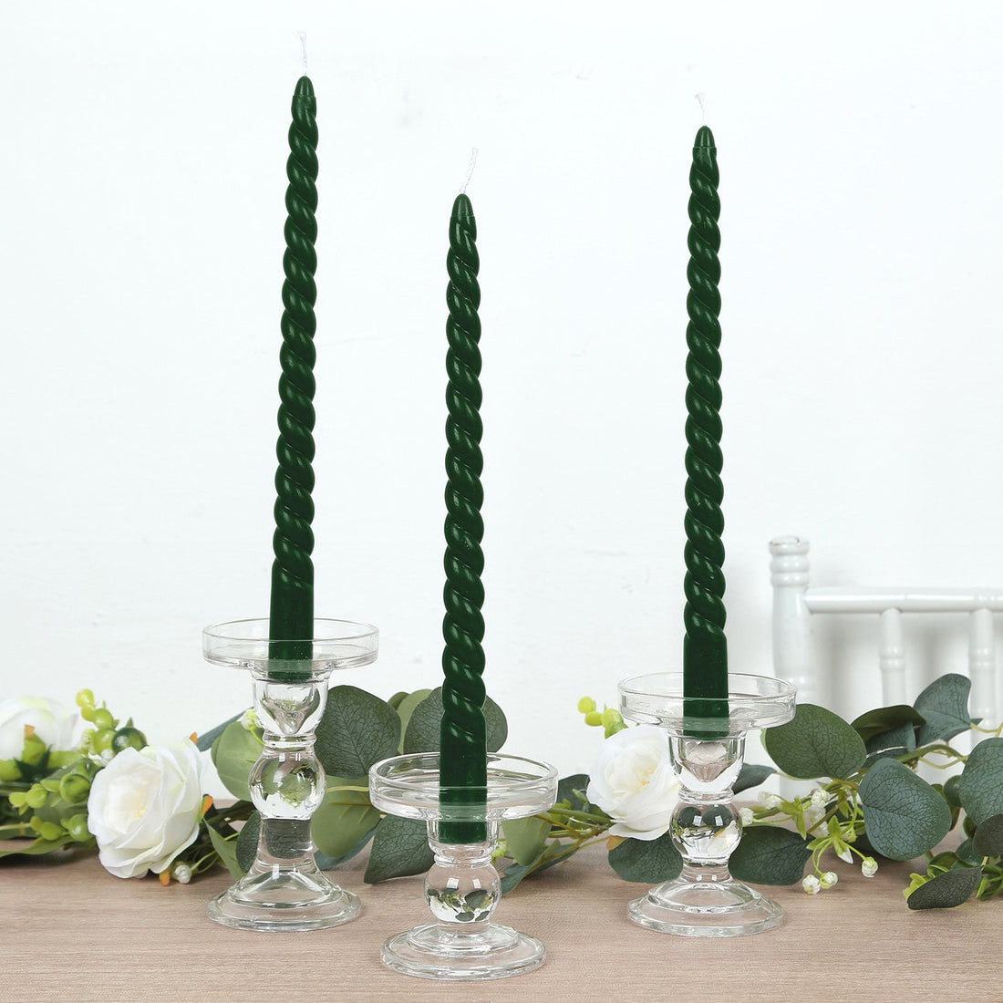 Three twisted green candles in clear glass holders with floral accents.