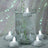 Floating candles in a decorative glass vase with greenery and a shimmering background.