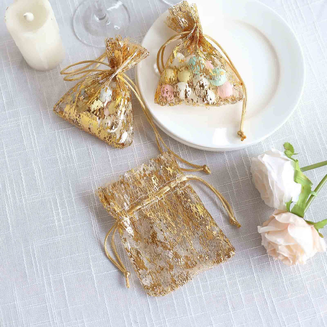 Gold organza gift bags with decorative candies on a white table setting.