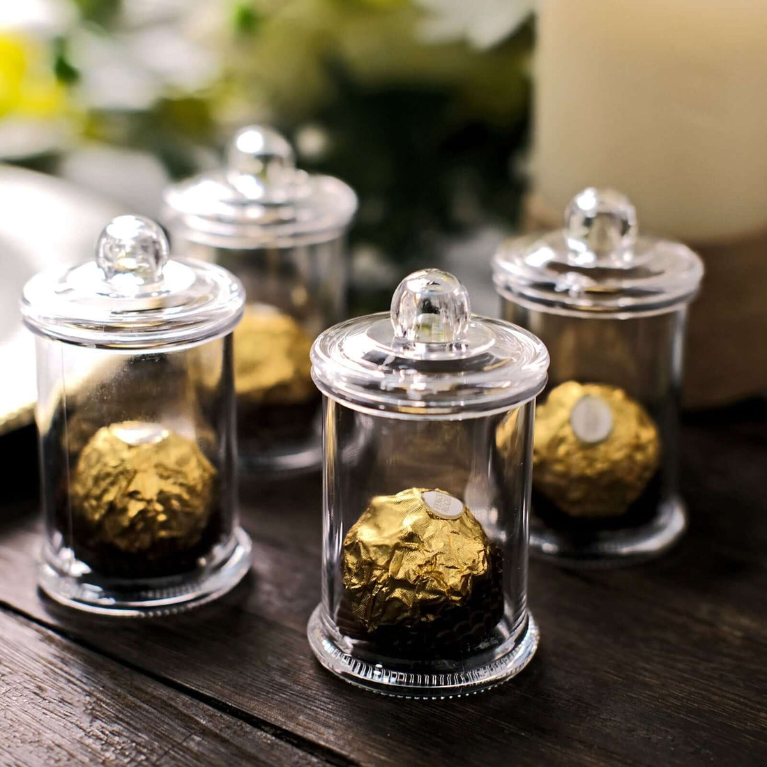 Glass jars with gold foil chocolates inside, elegantly displayed on a wooden table.