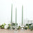 Green twisted candles in glass holders with floral accents.