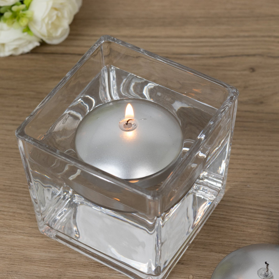 Silver candle in a clear glass holder on a wooden surface.
