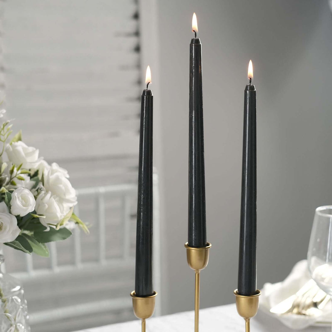 Three elegant black taper candles in gold holders on a stylish table setting.