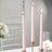 Pink taper candles in gold holders, elegantly lit for ambiance.