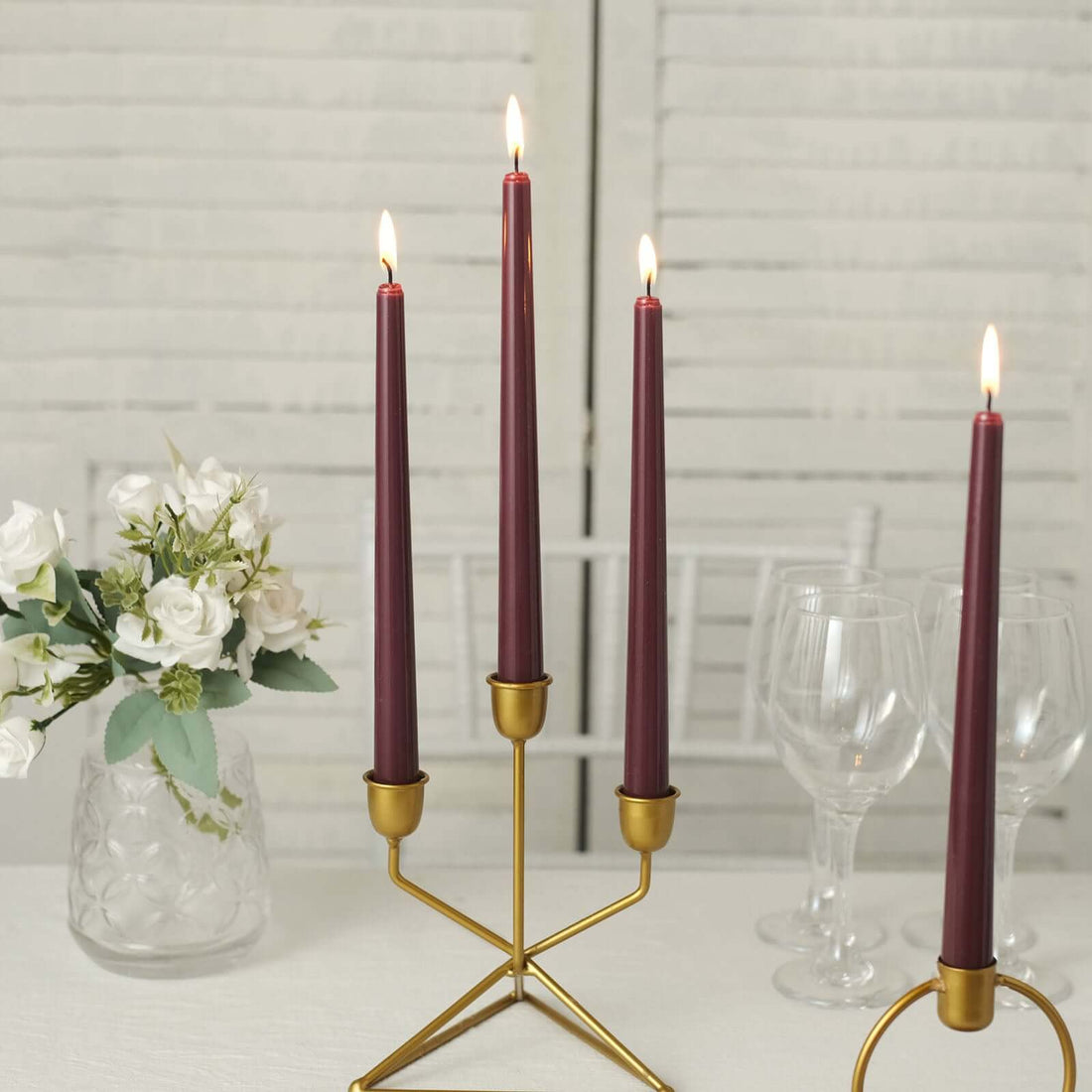 Elegant gold candle holder with burgundy candles and a floral centerpiece.