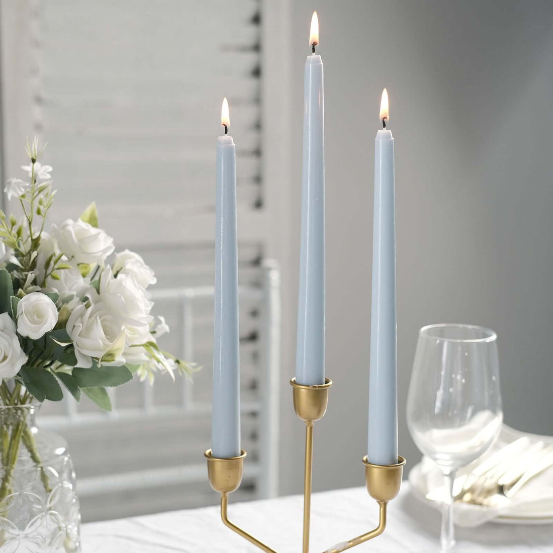 Elegant blue taper candles in a gold candle holder with white flowers and glassware.