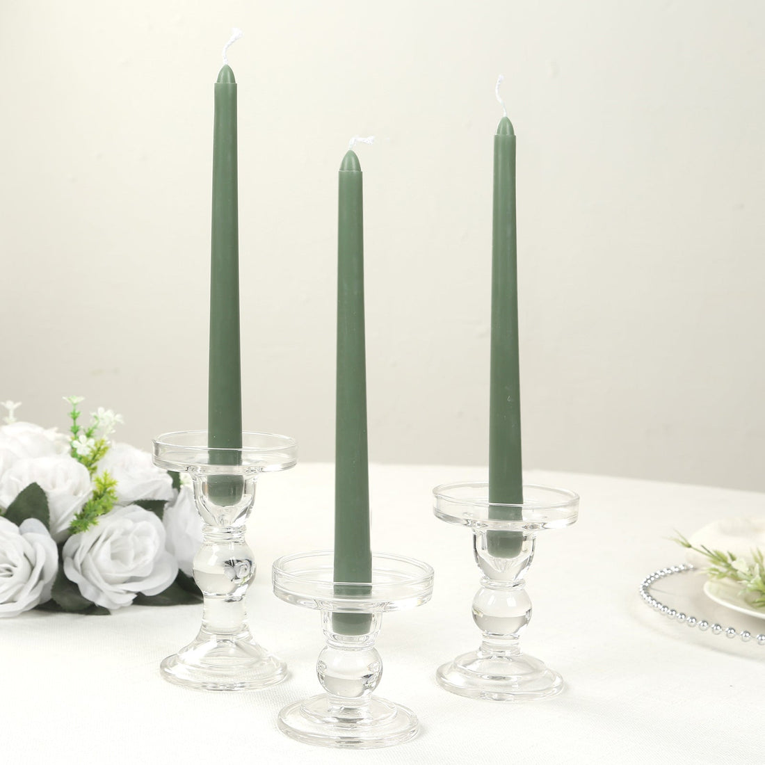 Green tapered candles in clear glass holders on a table with flowers.