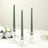 Green tapered candles in clear glass holders on a table with flowers.