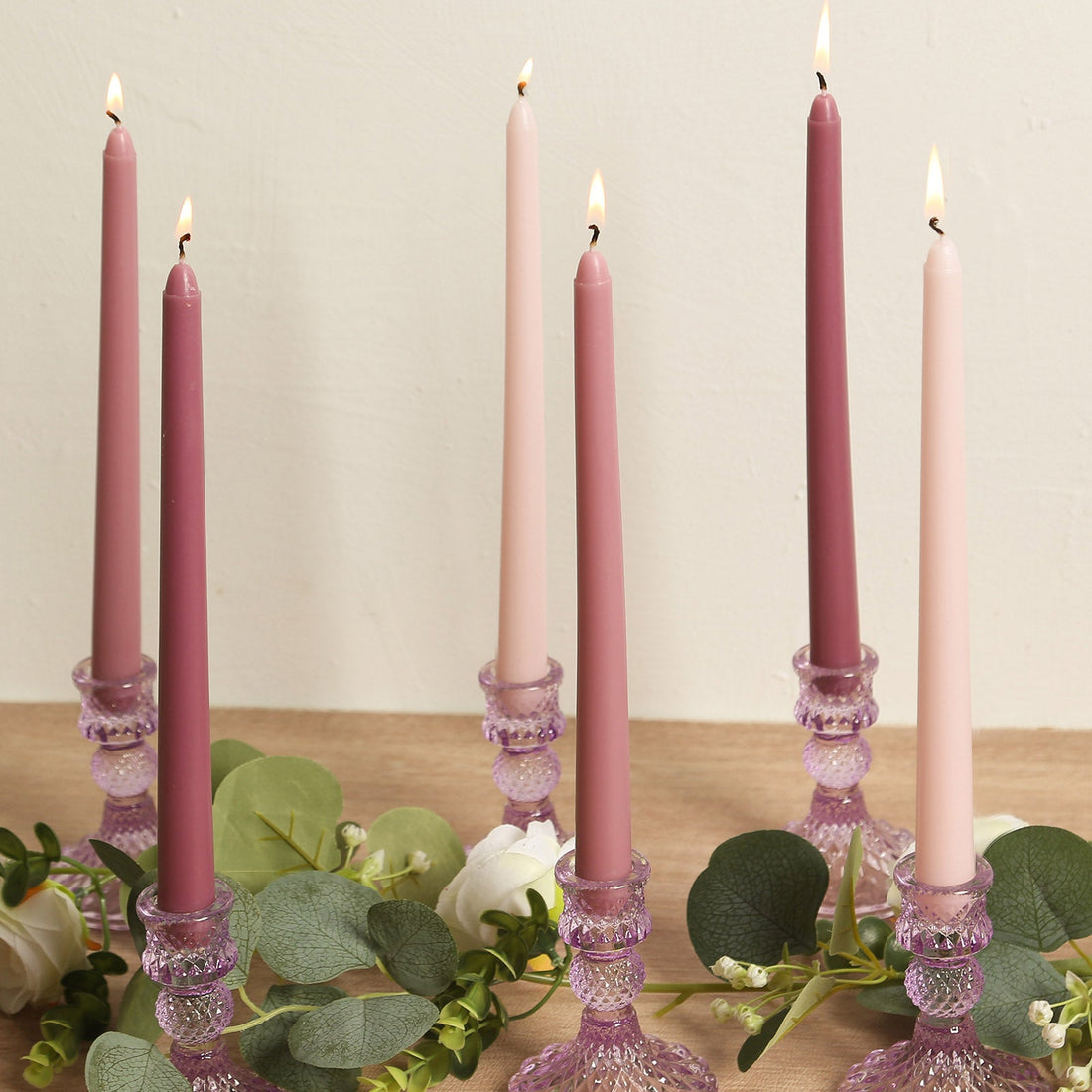 Elegant tapered candles in pastel shades with crystal holders and greenery accents.