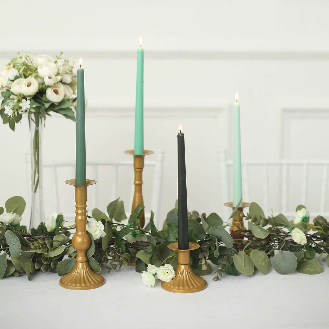 Elegant candle holders with colorful candles and greenery on a table setting.