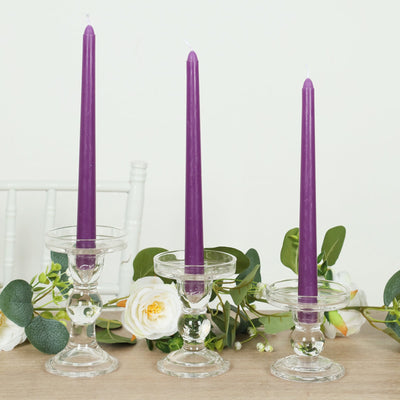 Purple tapered candles in glass holders with greenery decor.