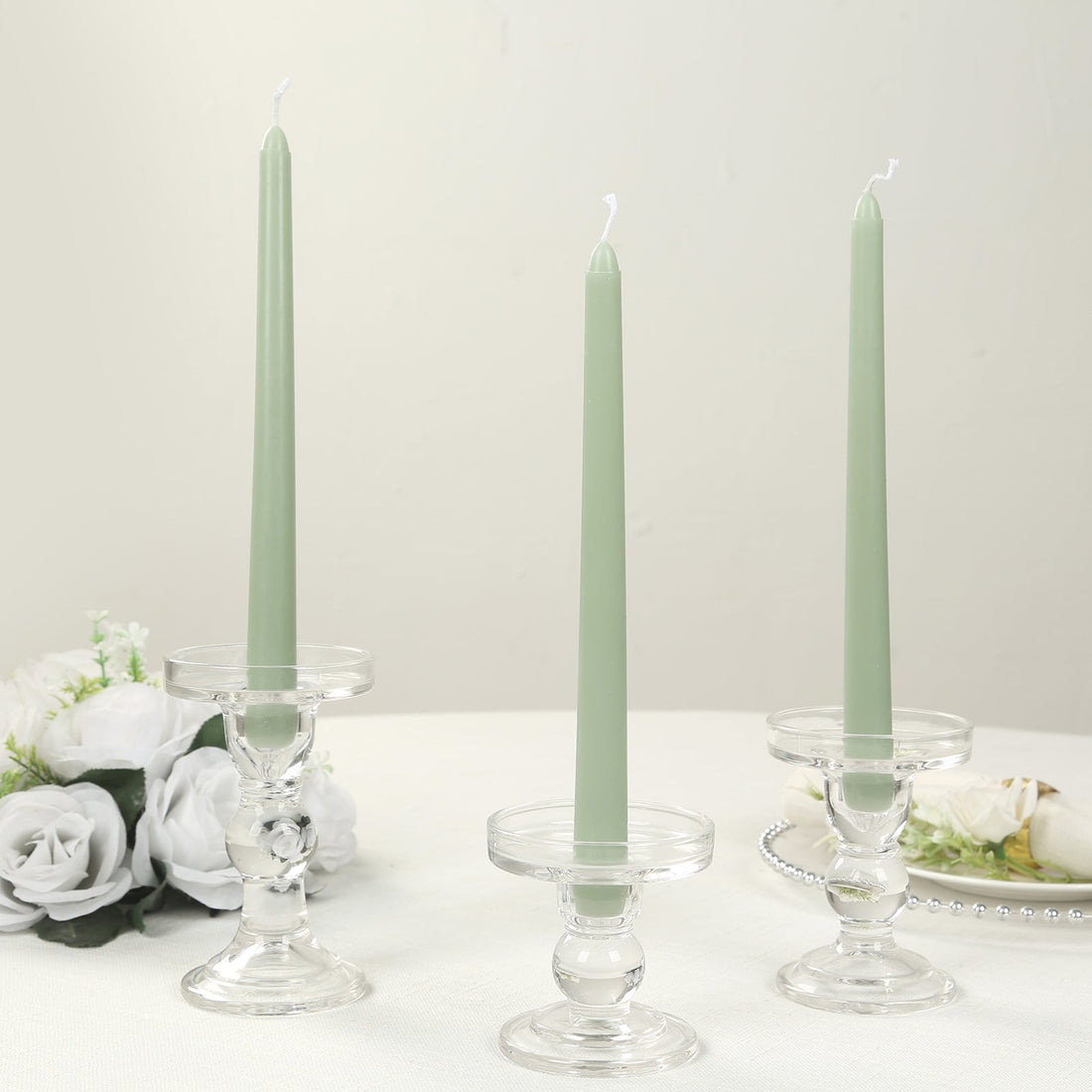 Three green taper candles in clear glass holders on a table.