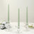 Three green taper candles in clear glass holders on a table.