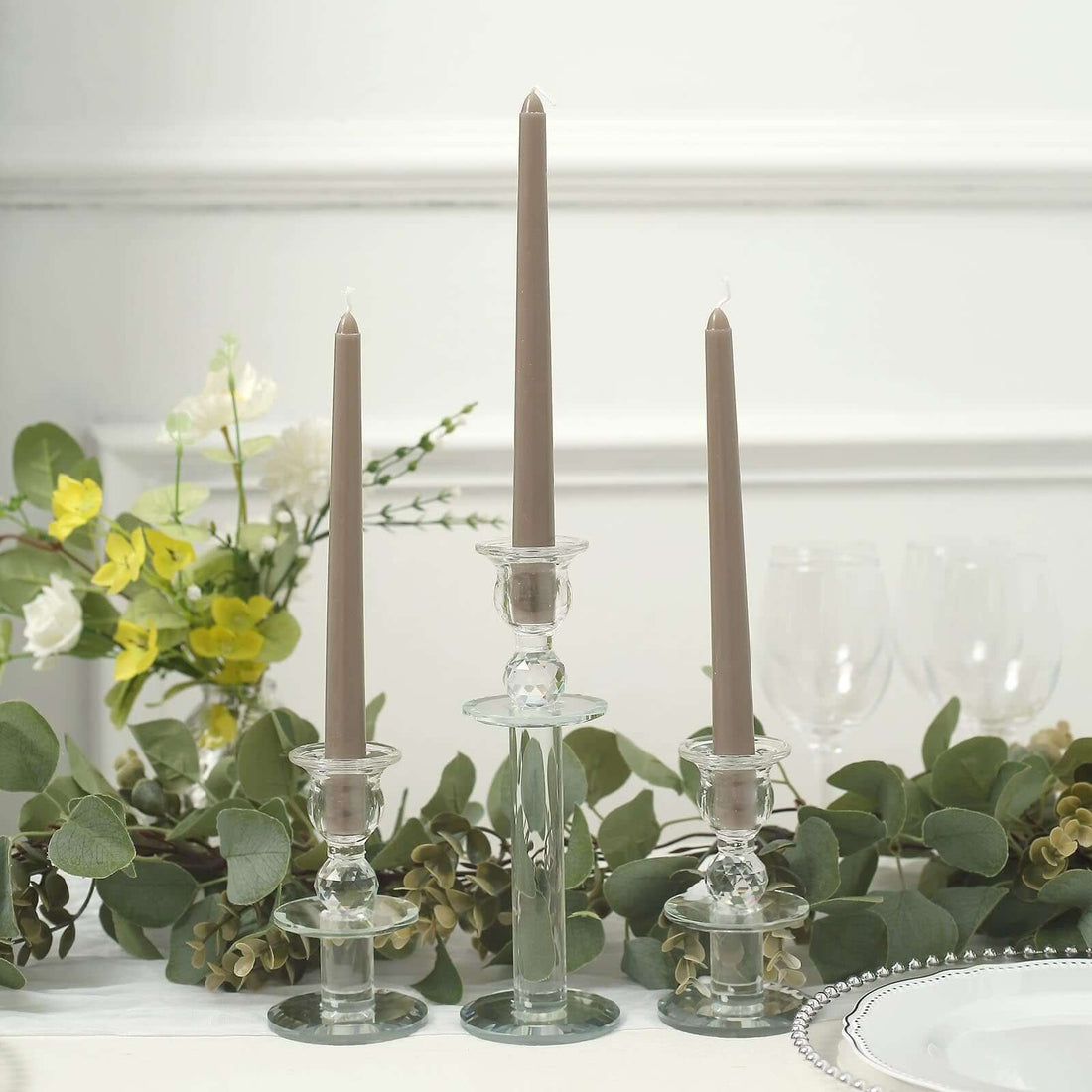 Elegant glass candlesticks with taper candles and greenery decor.