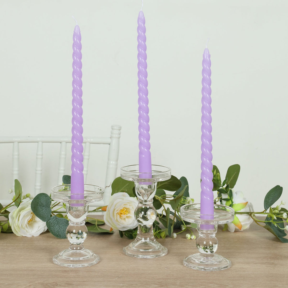 Purple twisted candles in elegant glass holders with floral decor.