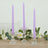 Purple twisted candles in elegant glass holders with floral decor.