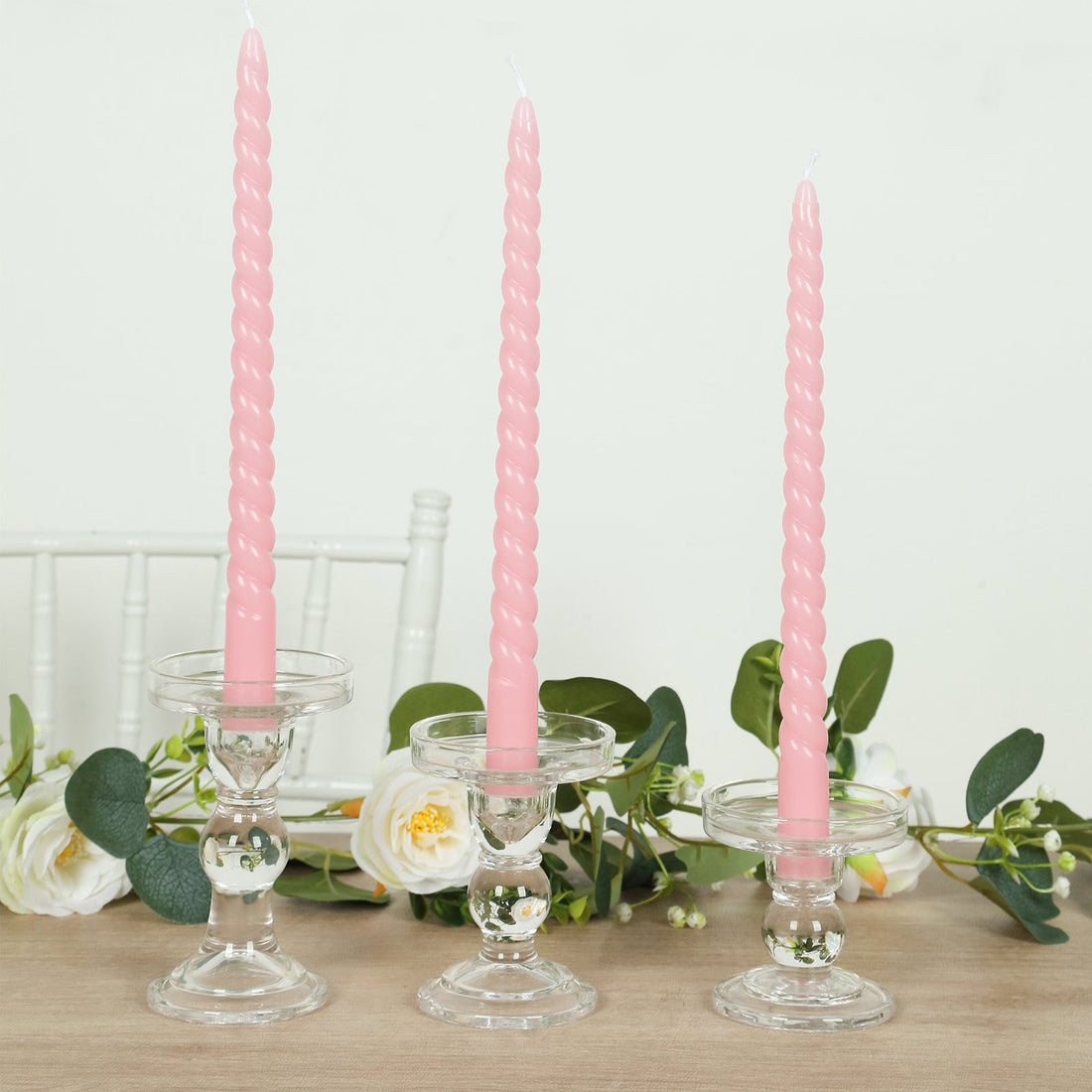 Pink twisted candles in glass holders with greenery and flowers.