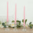 Pink twisted candles in glass holders with greenery and flowers.