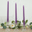 Three purple twisted candles in clear glass holders on a neutral table setting.