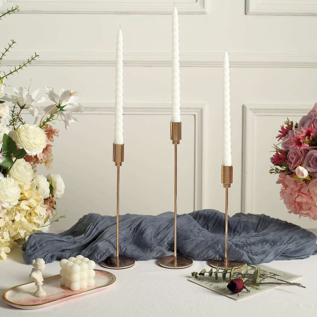 Elegant candle holders with white candles and floral arrangements on a table.