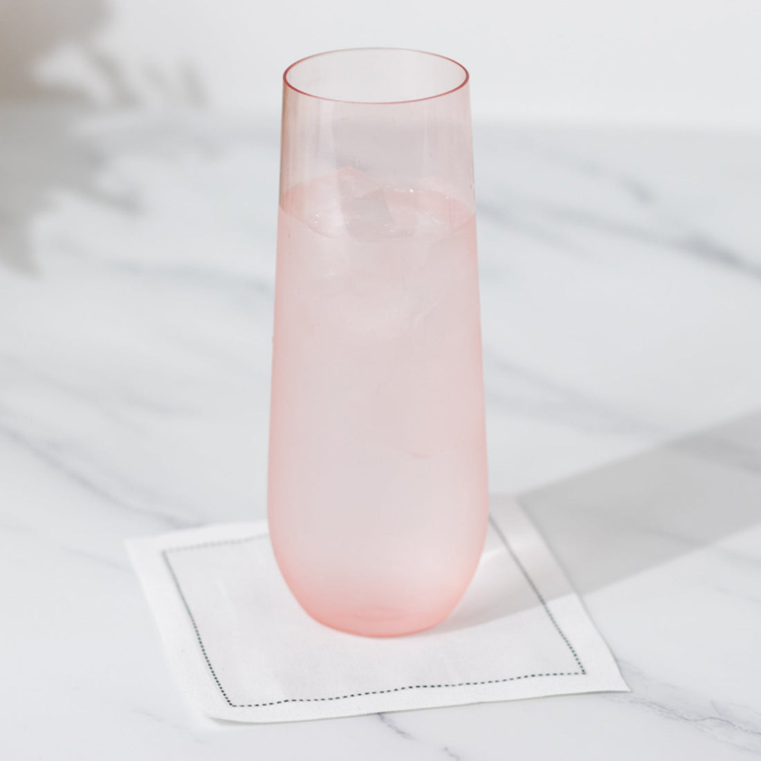 Pink glass with ice on a napkin against a marble surface.