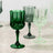 Colorful crystal glasses in green and clear on a neutral surface.