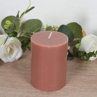 Pink pillar candle surrounded by greenery and white flowers.