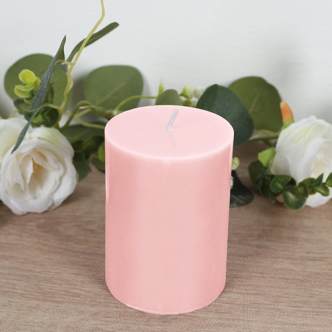Pink pillar candle surrounded by greenery and white flowers.