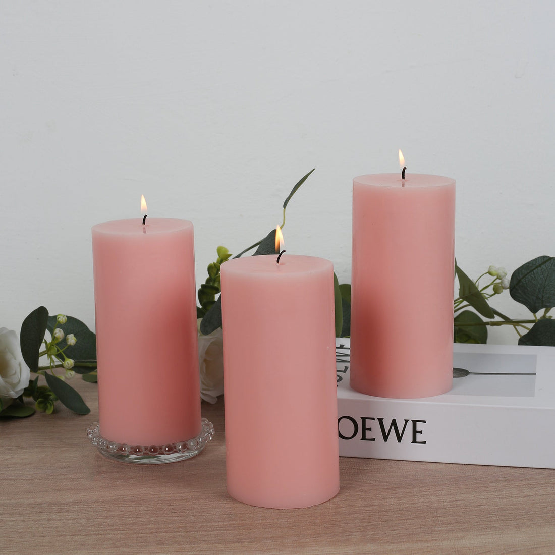 Three pink pillar candles with flames on a wooden surface.