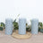 Set of three grey pillar candles on a woven mat with greenery accents.