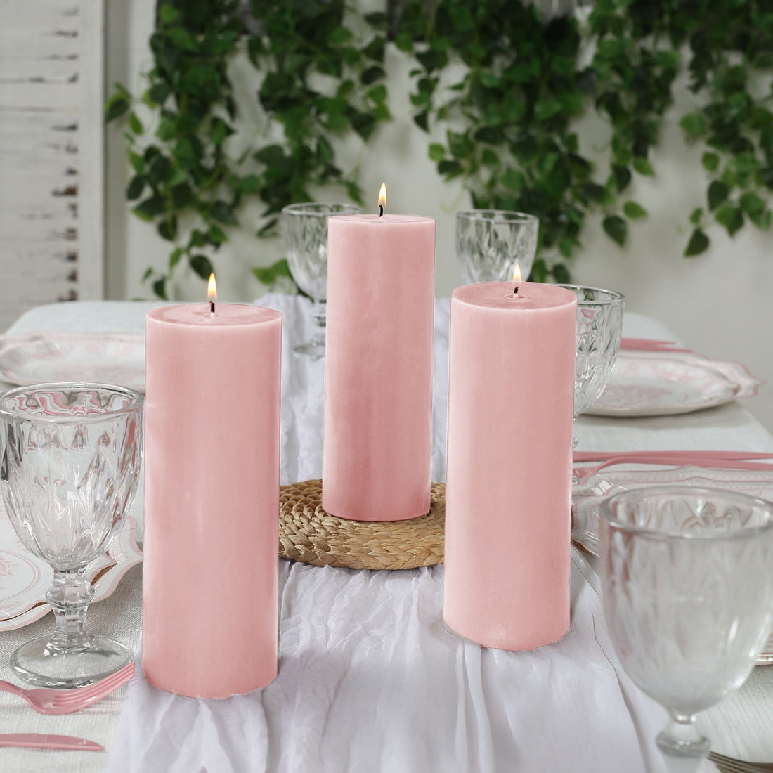 Pink pillar candles on a dining table with glassware and greenery decoration.
