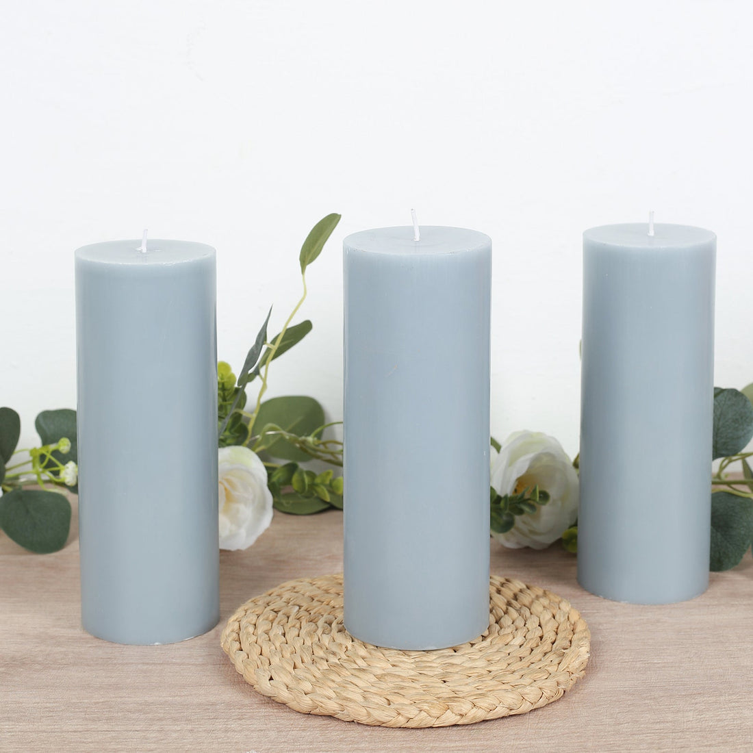 Set of three gray candles with decorative greenery on a woven mat.
