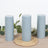 Set of three gray candles with decorative greenery on a woven mat.