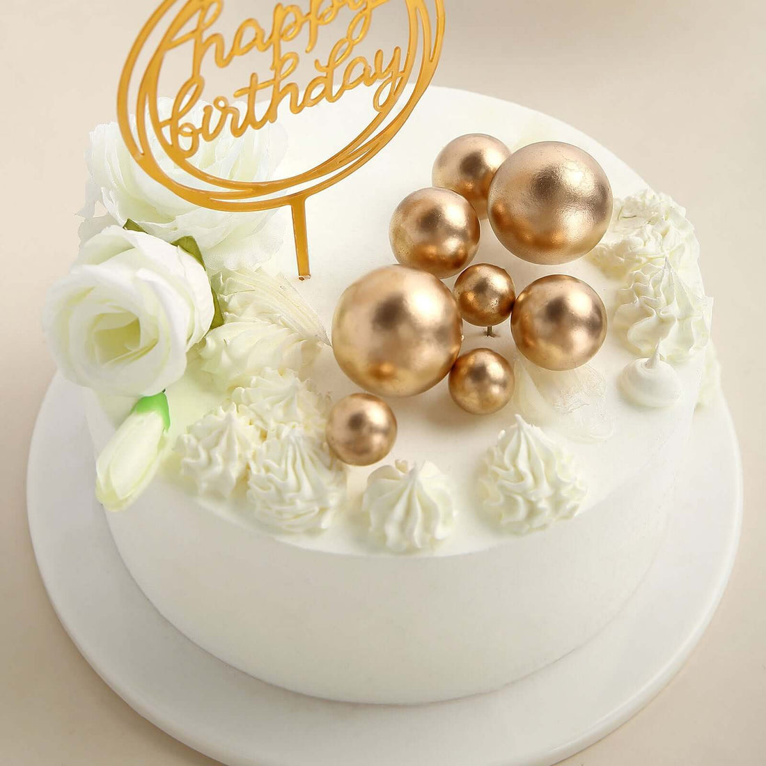 White birthday cake adorned with gold spheres and flowers.