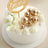 White birthday cake adorned with gold spheres and flowers.