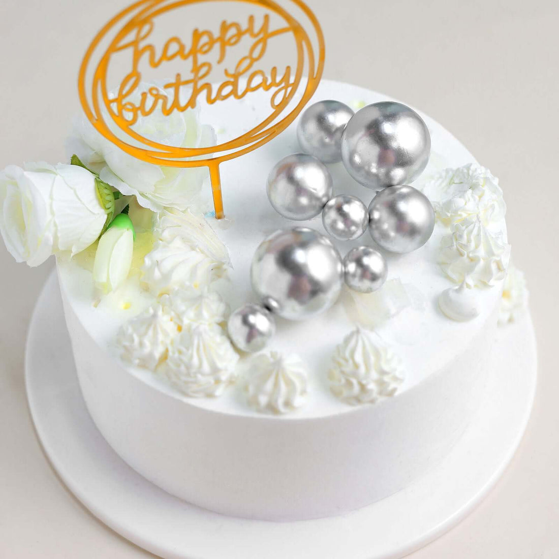 Birthday cake adorned with silver balls and white flowers.