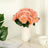 Pink rose bouquet in a white vase on a table with a plant and cup.