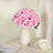 Pink rose bouquet in a white vase on a table with a cup and book.